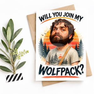 May include: A greeting card featuring a cartoon illustration of a bearded person with dark hair wearing a t-shirt with a forest graphic. The text reads WILL YOU JOIN MY WOLFPACK? The background shows a sunset, pine trees, and birds in flight.