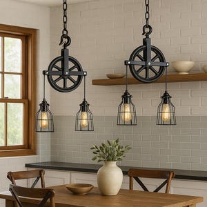 May include: Two black industrial-style pendant lights with a pulley design hang from the ceiling. Each light features a cage-like shade with a visible lightbulb. A wooden dining table and chairs are in the foreground.