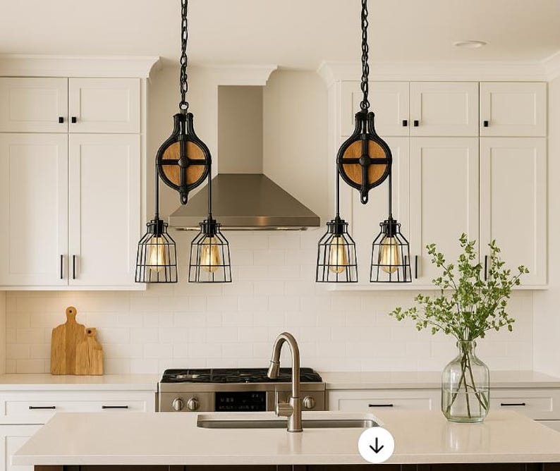 May include: Two black pendant lights with a cage design and Edison bulbs hang from the ceiling. The lights are suspended by a pulley system with a wooden wheel. The kitchen features white cabinets and a stainless steel extractor hood.