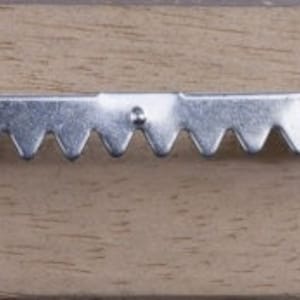 May include: A metal sawtooth picture hanger with two screws attached to a wooden surface. The hanger has a series of jagged teeth along its length, designed for secure wall mounting. The wood has a light brown color.