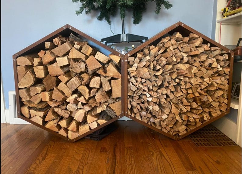 Puede incluir: Dos le&ntilde;eros hexagonales de madera marr&oacute;n oscuro, cada uno lleno de troncos partidos. Los soportes est&aacute;n unidos, creando una soluci&oacute;n de almacenamiento &uacute;nica para le&ntilde;a. Los troncos de madera son de varios tonos de marr&oacute;n.