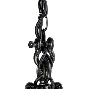May include: Close-up of a black industrial pendant light fitting. The fitting includes a heavy chain, a woven cord, and a pulley system. The metal components have a textured, matte finish, suggesting a vintage or rustic aesthetic.