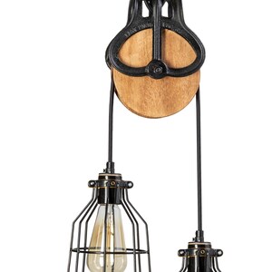 May include: Industrial pendant light with a black metal pulley system and two cage-style light fittings. The wooden pulley wheel and exposed light bulbs add a rustic touch. The light fittings are suspended from a chain.