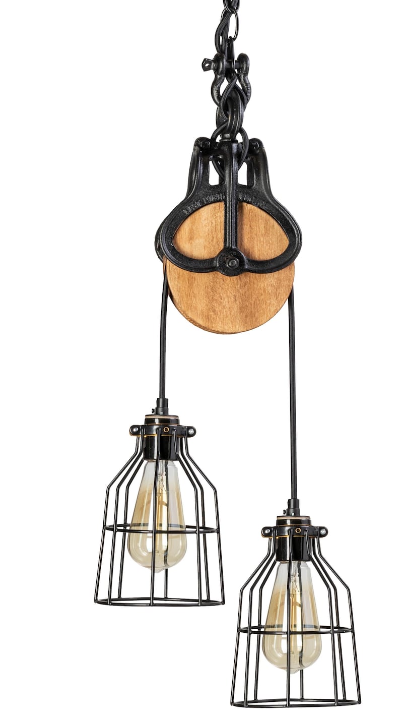 May include: Industrial pendant light with a black metal pulley system and two cage-style light fittings. The wooden pulley wheel and exposed light bulbs add a rustic touch. The light fittings are suspended from a chain.