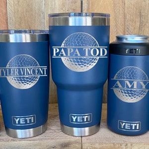 May include: Five Yeti tumblers with personalized names and a golf ball design. The tumblers are in various sizes and are all blue with silver accents.