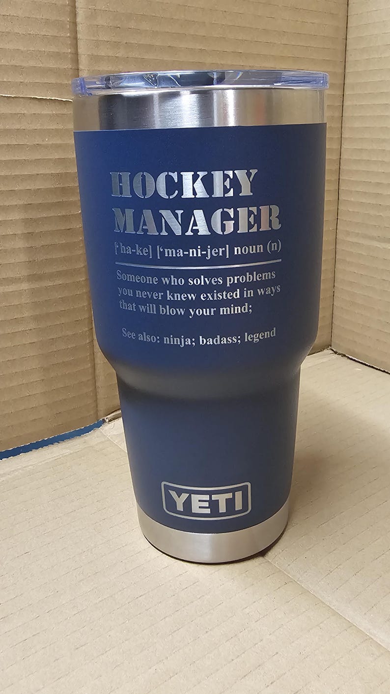 May include: A blue YETI tumbler with a stainless steel lid and a silver inscription that reads "HOCKEY MANAGER [ha-ke] ['ma-ni-jer] noun (n) Someone who solves problems you never knew existed in ways that will blow your mind: See also: ninja; badass; legend"
