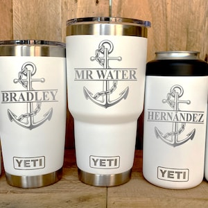 May include: Five white Yeti tumblers with a silver anchor and personalized names. The tumblers are in different sizes, including a slim can insulator.
