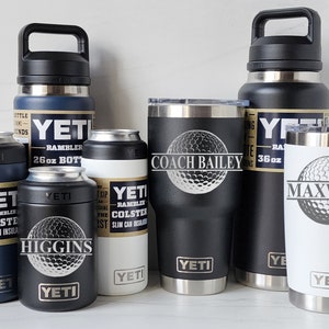 May include: A collection of six YETI brand insulated drinkware items, including a 36 oz Rambler bottle, a 26 oz Rambler bottle, a 20 oz Rambler tumbler, and three Rambler Colsters. The tumblers and bottles are personalized with a golf ball design and names.