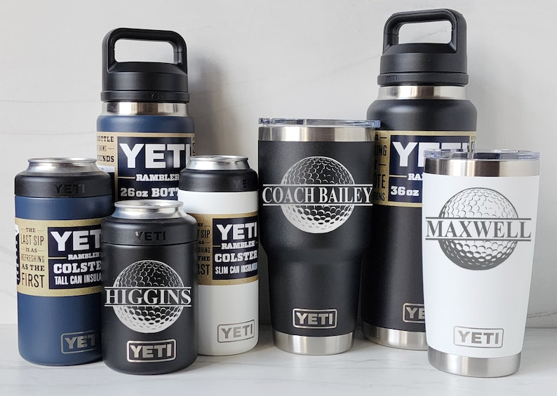 May include: A collection of six YETI brand insulated drinkware items, including a 36 oz Rambler bottle, a 26 oz Rambler bottle, a 20 oz Rambler tumbler, and three Rambler Colsters. The tumblers and bottles are personalized with a golf ball design and names.