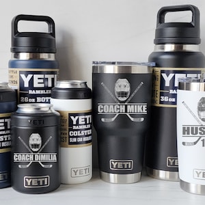 May include: A collection of six Yeti brand insulated drinkware items. The items include a 26 ounce bottle, a 36 ounce bottle, two 12 ounce tumblers, and two 12 ounce slim can insulators. The tumblers and can insulators are personalized with hockey-themed designs and names.