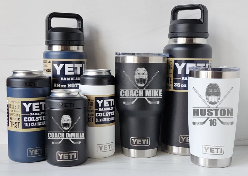 May include: A collection of six Yeti brand insulated drinkware items. The items include a 26 ounce bottle, a 36 ounce bottle, two 12 ounce tumblers, and two 12 ounce slim can insulators. The tumblers and can insulators are personalized with hockey-themed designs and names.