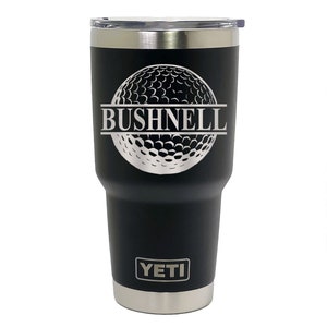 May include: Black Yeti tumbler with a silver golf ball design and the text "BUSHNELL" engraved on it.