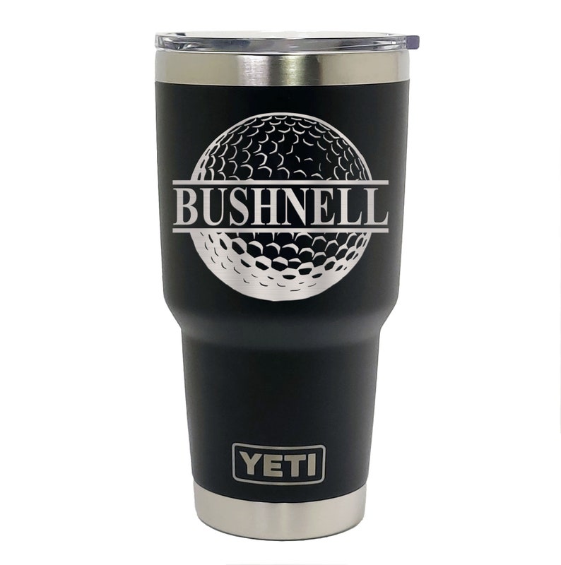 May include: Black Yeti tumbler with a silver golf ball design and the text "BUSHNELL" engraved on it.