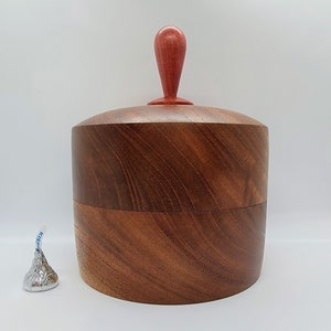 May include: A wooden box with a red knob on the lid. The box is made of dark wood with a natural grain pattern.