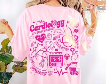 May include: Pink t-shirt with a graphic design of a heart and medical symbols. The text on the shirt reads "Cardiology is a work of heart".
