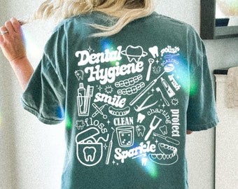 Może przedstawiać: Koszulka w kolorze turkusowym z białym nadrukiem przedstawiającym narzędzia do higieny jamy ustnej i tekst "Dental Hygiene" wraz z innymi słowami, takimi jak "smile", "floss", "clean", "sparkle", "polish", "charting", "protect" i "brush".