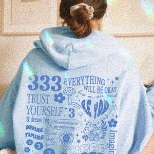 May include: Light blue hoodie with a graphic print featuring the text "333 EVERYTHING WILL BE OKAY TRUST YOURSELF: 3 & dream big DIVING TIMING" and various illustrations including flowers, mushrooms, and stars.
