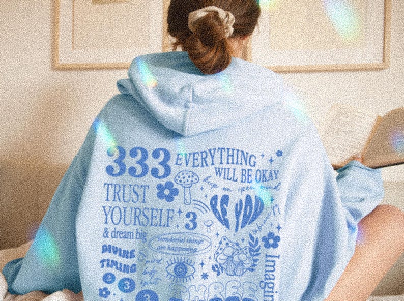 May include: Light blue hoodie with a graphic print featuring the text "333 EVERYTHING WILL BE OKAY TRUST YOURSELF: 3 & dream big DIVING TIMING" and various illustrations including flowers, mushrooms, and stars.