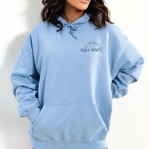Puede incluir: Sudadera azul claro con capucha y cord&oacute;n ajustable, y bolsillo delantero. El texto "is the best lake life" est&aacute; impreso en azul m&aacute;s oscuro en el pecho. La sudadera es de material suave.