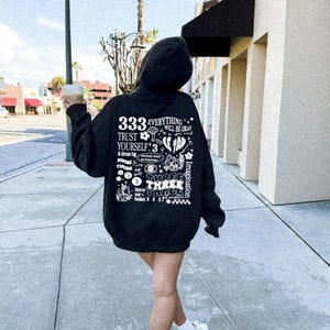 May include: Black hoodie with a white graphic print on the back. The graphic features the number 333, the words "everything will be okay", "trust yourself", and "imagination".