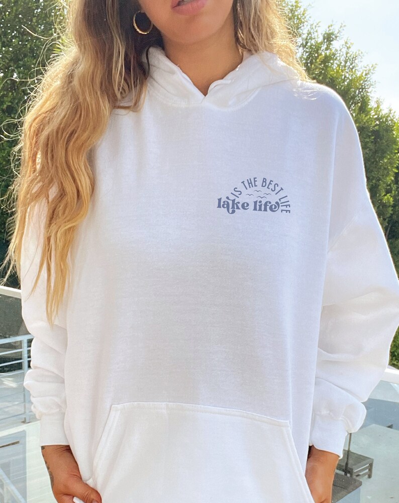 Puede incluir: Sudadera con capucha blanca con bolsillo delantero y capucha. El texto "lake life is the best life" est&aacute; impreso en azul en el pecho. La sudadera con capucha est&aacute; hecha de un material suave.