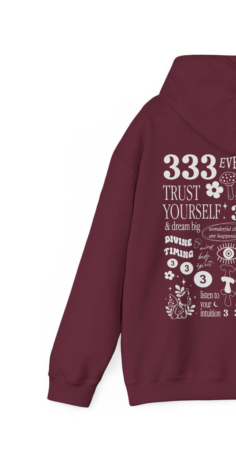 May include: Burgundy hoodie with a white graphic print that says "333 EVE TRUST YOURSELF! & dream big DIVINE TIMING 333 listen to your intuition 3" with illustrations of mushrooms, flowers, and a crescent moon.