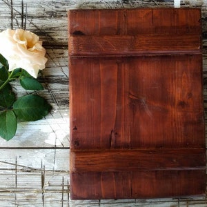 May include: A rustic wooden sign with a dark brown stain. The sign is made of planks of wood with a natural grain pattern. The sign is sitting on a whitewashed wooden surface.