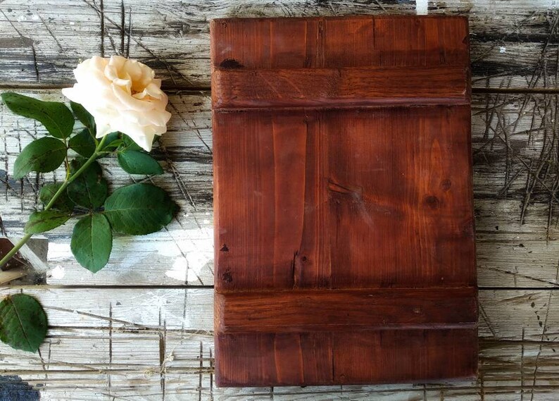 May include: A rustic wooden sign with a dark brown stain. The sign is made of planks of wood with a natural grain pattern. The sign is sitting on a whitewashed wooden surface.