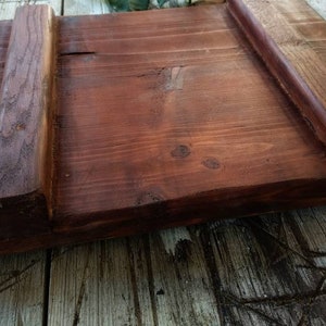 May include: A wooden cutting board with two raised edges on the sides. The board is stained a dark reddish brown color.