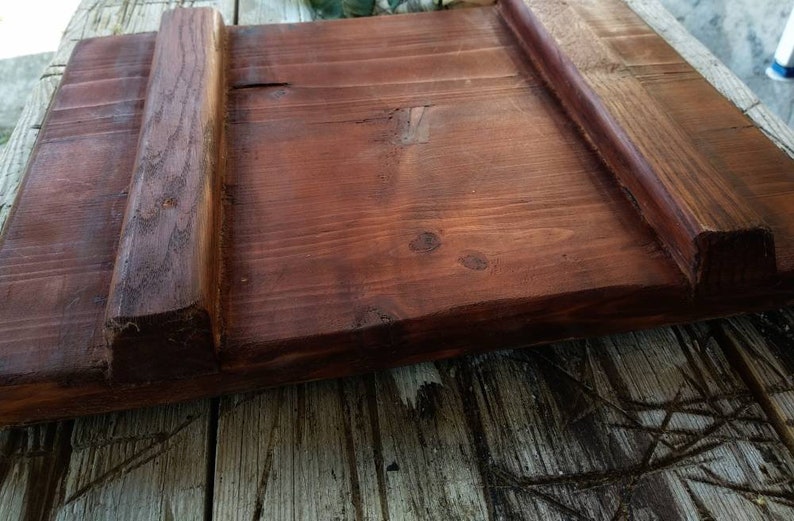 May include: A wooden cutting board with two raised edges on the sides. The board is stained a dark reddish brown color.