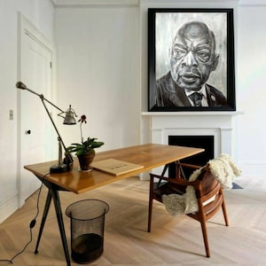 以下が含まれることがあります： スーツを着た男性の白黒肖像画が、黒い金属製の椅子のある木製デスクの上に飾られています。デスクには黒い金属製のランプと鉢植えの植物が置かれています。部屋は白い壁と白い暖炉があります。