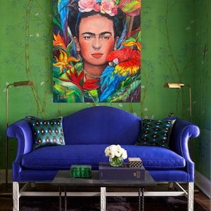 Pu&ograve; includere: Un divano in velluto blu con gambe bianche e un tavolino da caff&egrave; nero. Il divano ha due cuscini con un motivo verde e blu. Un dipinto di Frida Kahlo con pappagalli e fiori &egrave; appeso al muro dietro il divano.