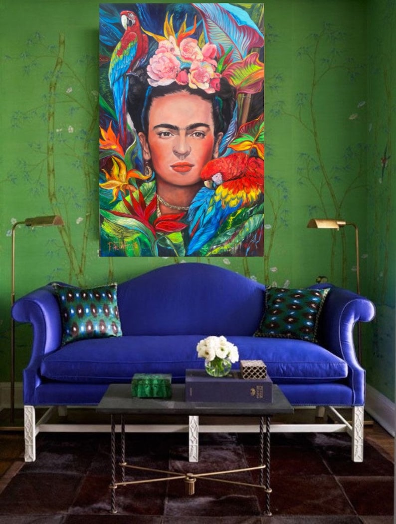 Pu&ograve; includere: Un divano in velluto blu con gambe bianche e un tavolino da caff&egrave; nero. Il divano ha due cuscini con un motivo verde e blu. Un dipinto di Frida Kahlo con pappagalli e fiori &egrave; appeso al muro dietro il divano.