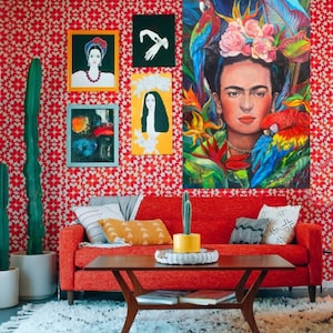 Pu&ograve; includere: Un divano rosso con cuscini gialli e grigi si trova di fronte a una parete rossa con un motivo geometrico. La parete &egrave; decorata con opere d'arte incorniciate, tra cui un dipinto di Frida Kahlo con pappagalli.