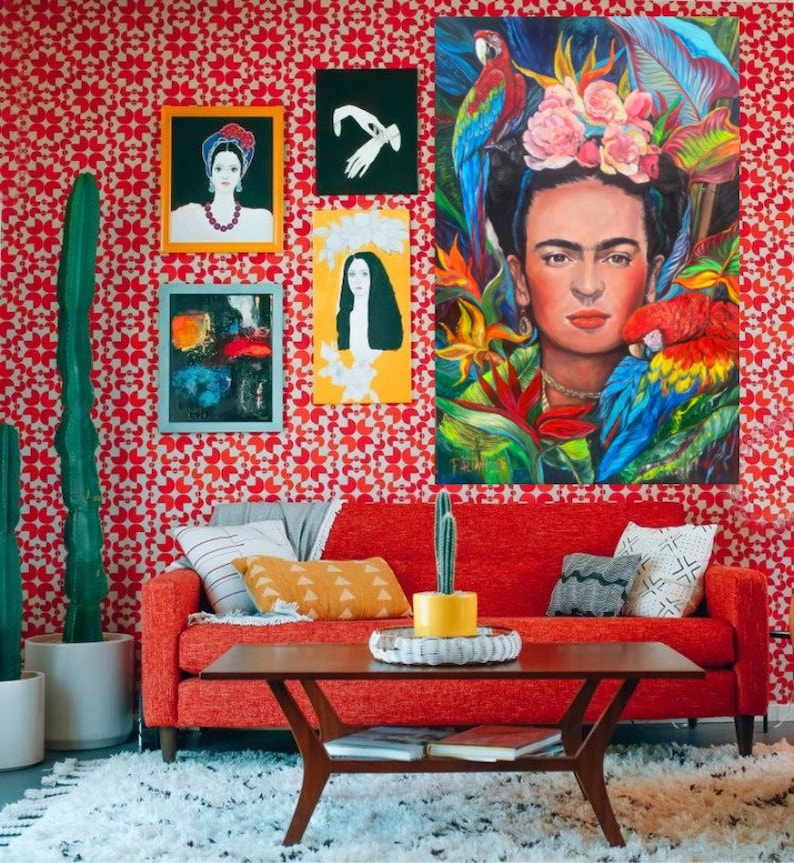 Pu&ograve; includere: Un divano rosso con cuscini gialli e grigi si trova di fronte a una parete rossa con un motivo geometrico. La parete &egrave; decorata con opere d'arte incorniciate, tra cui un dipinto di Frida Kahlo con pappagalli.