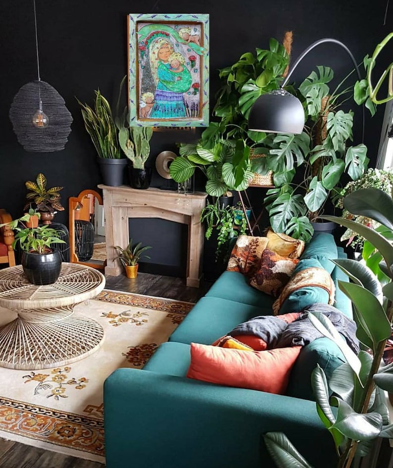 May include: A teal green sofa with a variety of throw pillows in a living room with a fireplace and many plants. The artwork above the fireplace is a painting of a woman holding a child.