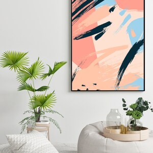 May include: Abstract art print featuring black, pink and blue brushstrokes, framed in black. The print is hanging on a white wall above a white beanbag chair.