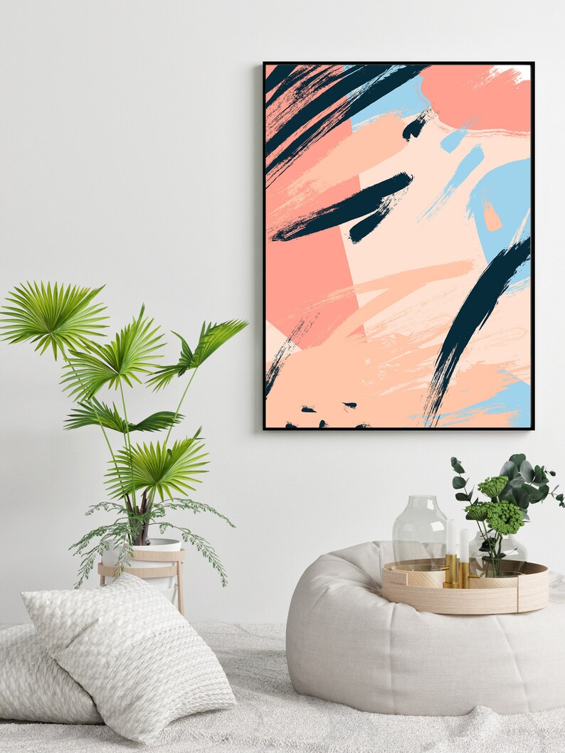 May include: Abstract art print featuring black, pink and blue brushstrokes, framed in black. The print is hanging on a white wall above a white beanbag chair.
