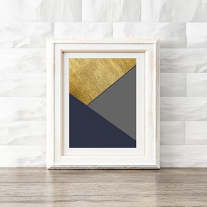 Könnte beinhalten: Ein gerahmter abstrakter geometrischer Druck in Gold, Grau und Marineblau. Der Druck ist in einem weißen Rahmen.