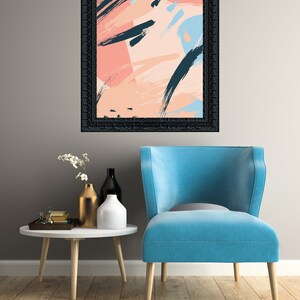 May include: A blue armchair with a black framed abstract painting with pink, blue, and black brushstrokes hanging above it. The armchair is in front of a white table with a gold vase and two white vases with flowers.