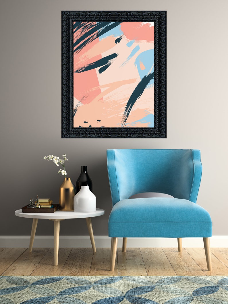 May include: A blue armchair with a black framed abstract painting with pink, blue, and black brushstrokes hanging above it. The armchair is in front of a white table with a gold vase and two white vases with flowers.