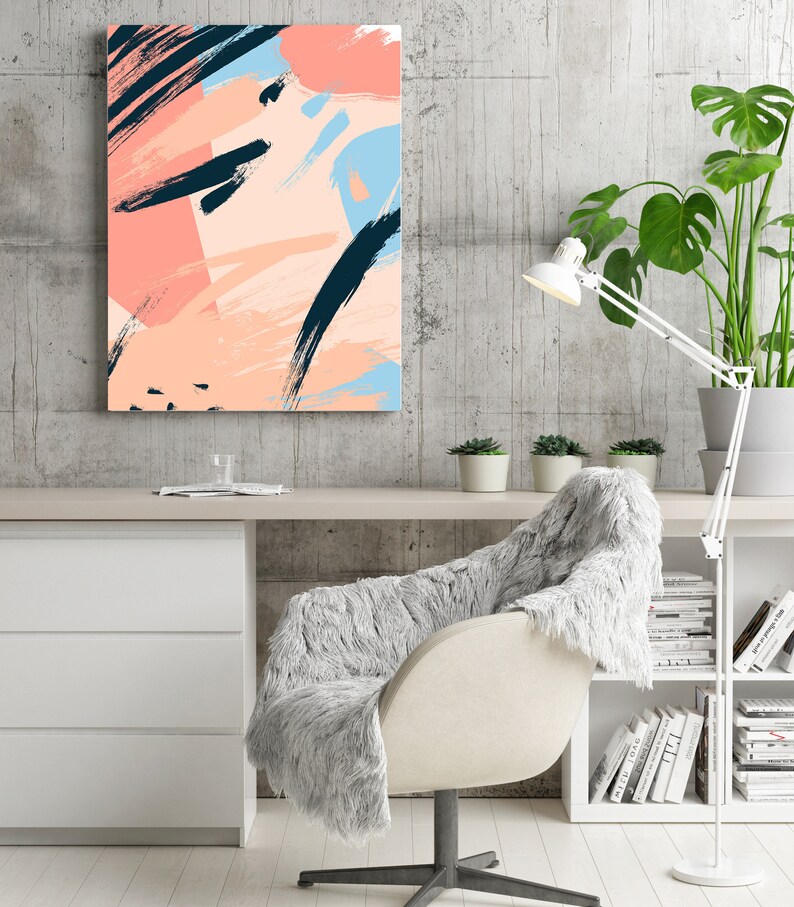 May include: Abstract art print featuring pink, blue, and black brushstrokes on a white background. The print is hanging on a grey wall above a white desk with a white chair and a bookshelf.
