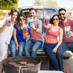 May include: A group of friends enjoying drinks from colourful pouches with the word "TEAM" printed on them. They are sitting in the back of a pick-up truck with a grill in the foreground.