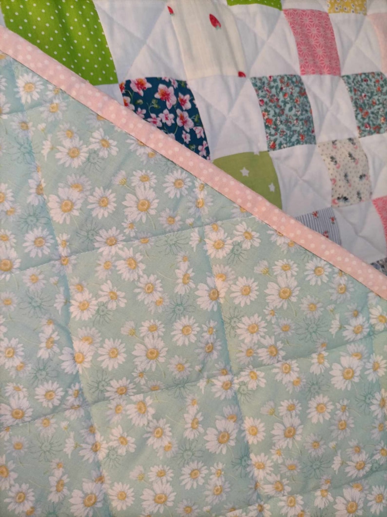 May include: A patchwork quilt with a green, white, and pink floral pattern. The quilt is made of squares of different fabrics and is quilted with a diamond pattern. The quilt is edged with a pink and white polka dot trim.