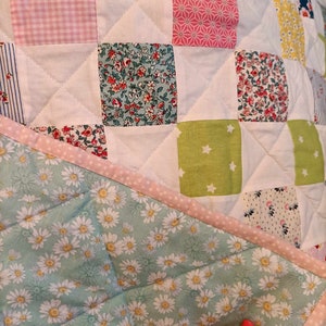 Peut inclure: Une courtepointe en patchwork avec une variété de motifs floraux et géométriques en rose, vert, blanc et bleu. La courtepointe est faite de carrés et a un fond blanc.