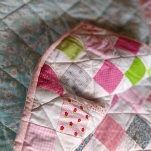 May include: A patchwork quilt with a variety of pink, green, and white fabrics. The quilt is made of squares and has a quilted texture.