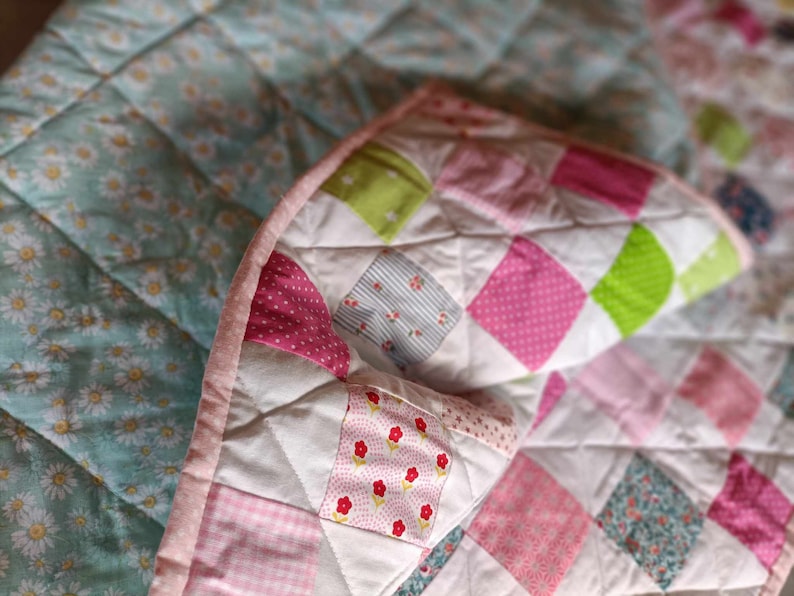 May include: A patchwork quilt with a variety of pink, green, and white fabrics. The quilt is made of squares and has a quilted texture.