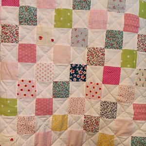 May include: A white quilt with a patchwork design. The quilt is made up of squares of different fabrics, each with a different pattern. The patterns include floral prints, polka dots, stripes, and geometric designs. The quilt is quilted in a diamond pattern.