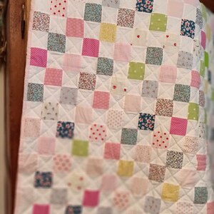 May include: A white patchwork quilt with squares of various floral and patterned fabrics in pink, green, blue, and yellow.