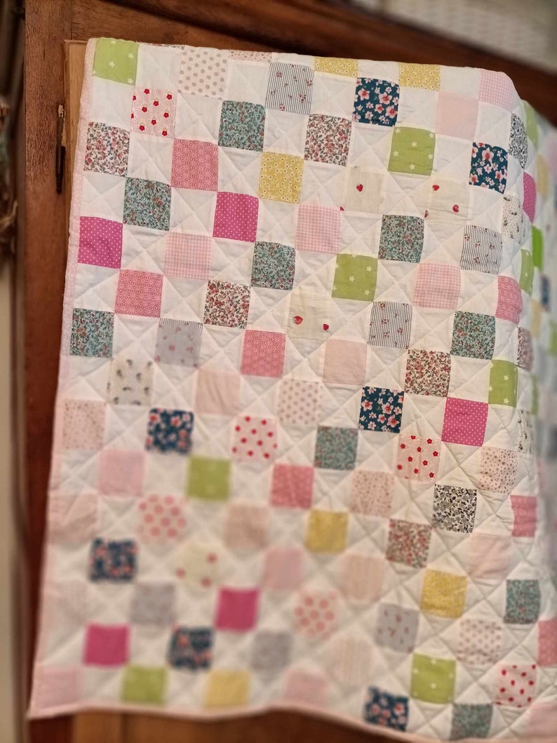 May include: A white patchwork quilt with squares of various floral and patterned fabrics in pink, green, blue, and yellow.